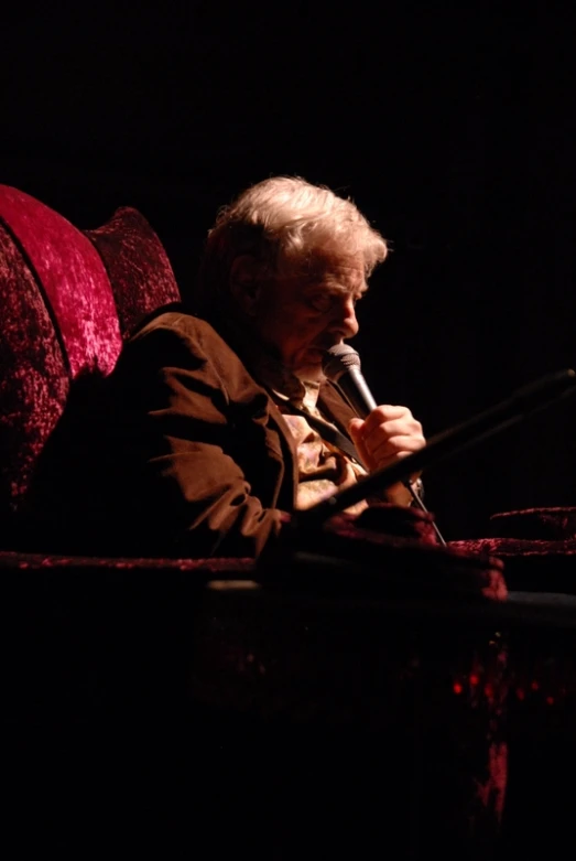 older man in dark room talking into a microphone