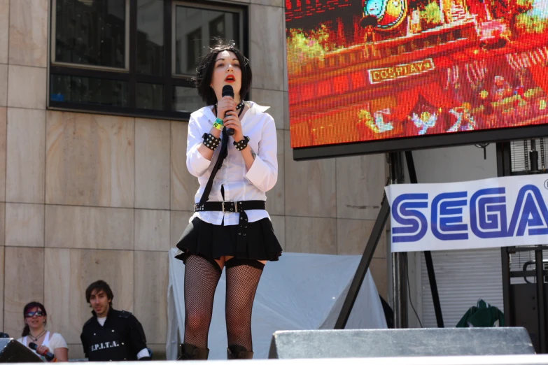 a woman with black hair and a skirt on sings into a microphone