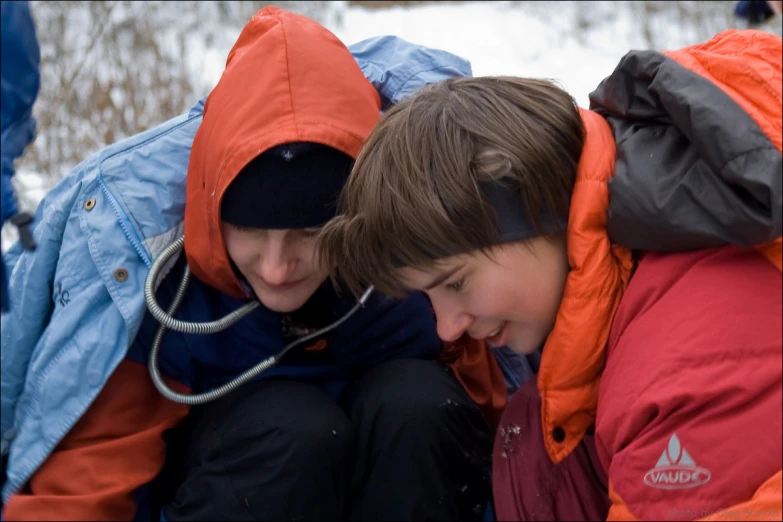 two young men, wearing jackets and beanies, crouching together