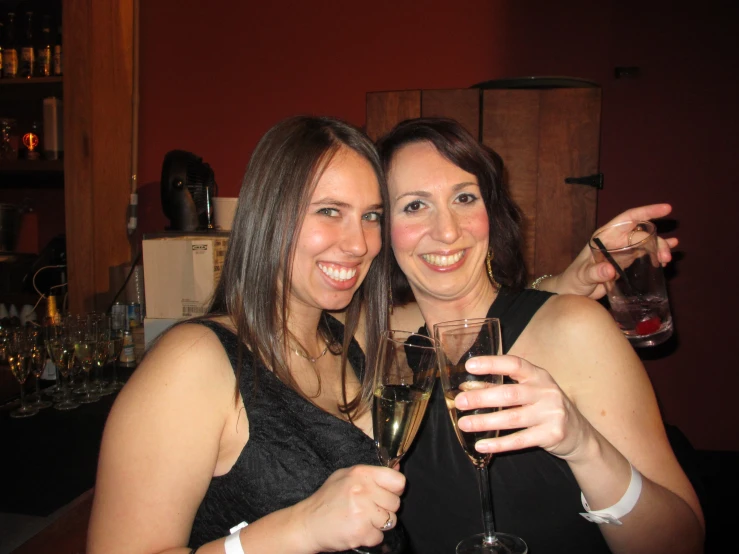 two women are smiling while holding up glasses