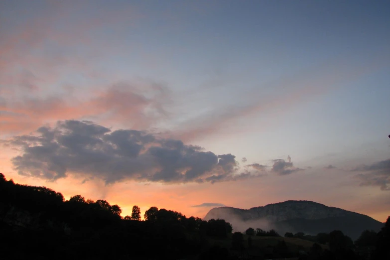 the sun sets as clouds cover a mountain