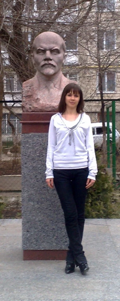 a woman stands near a statue of a person with an evil face