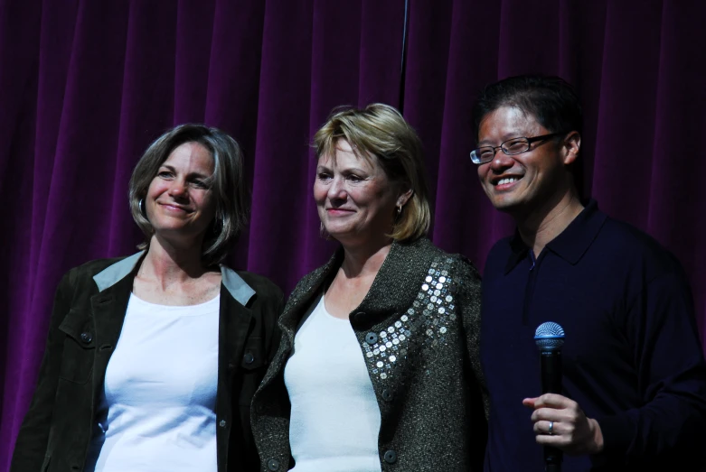 three smiling people pose for a po while holding a microphone