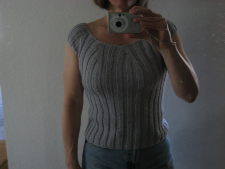 a woman takes a selfie in a mirror wearing a sweater and jeans