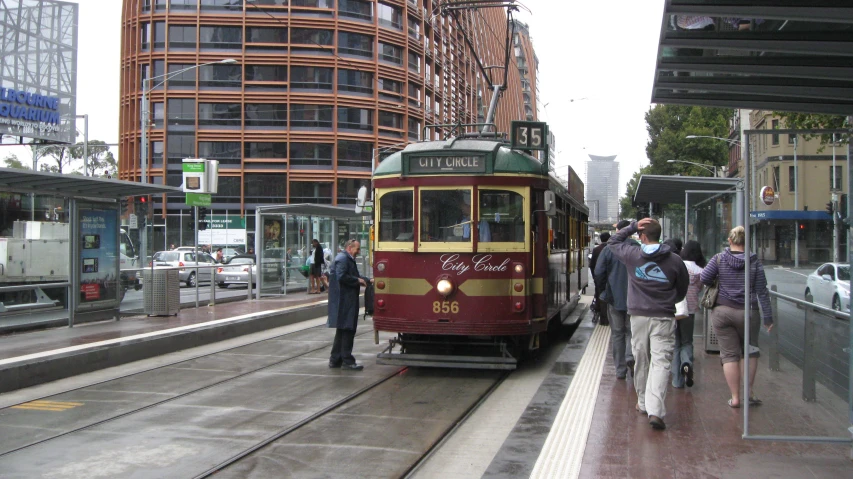 a tram in the street in front of people walking on the sidewalk