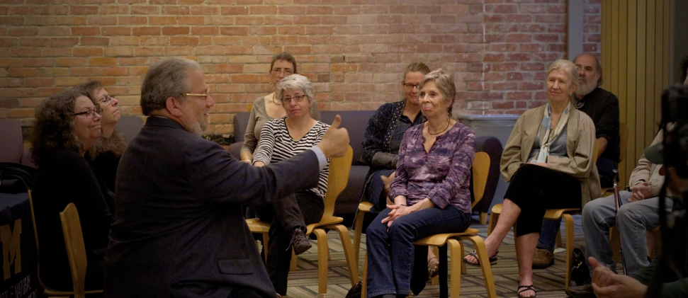 several people sitting down in chairs in front of a brick wall