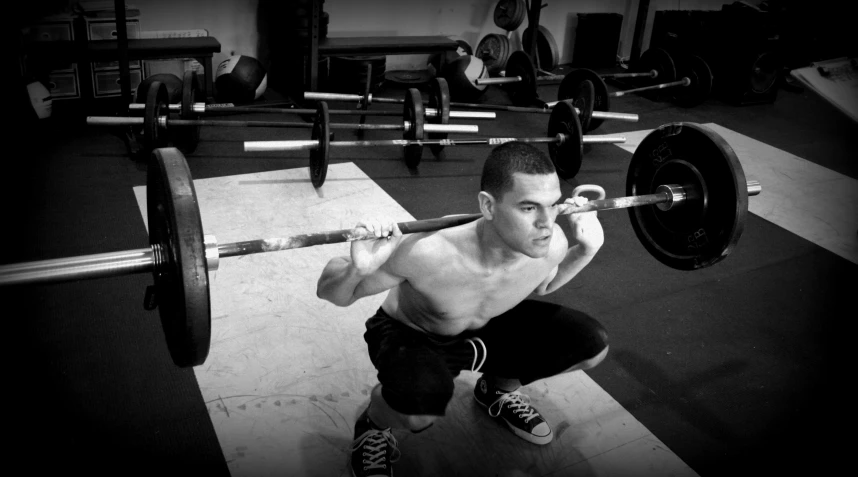 a young man in the gym squatting on a barbell