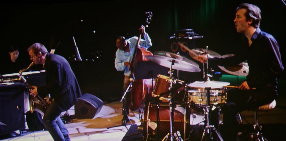 a man standing next to a man sitting on top of a drum set