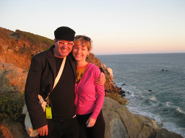 a woman and man taking a selfie on a rocky cliff near the ocean