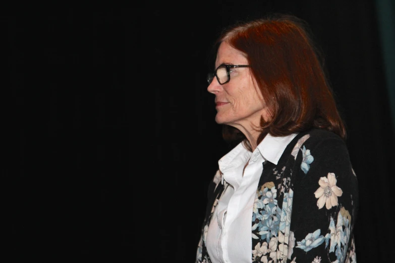 the woman wearing glasses stands in front of a black background