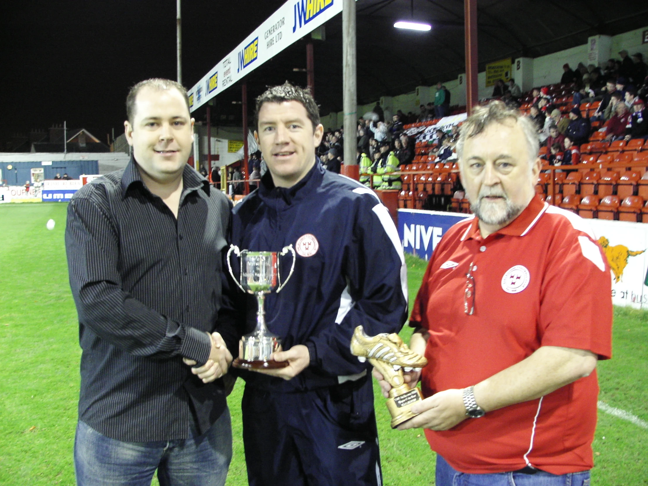 three men posing with trophy cups on a grass field