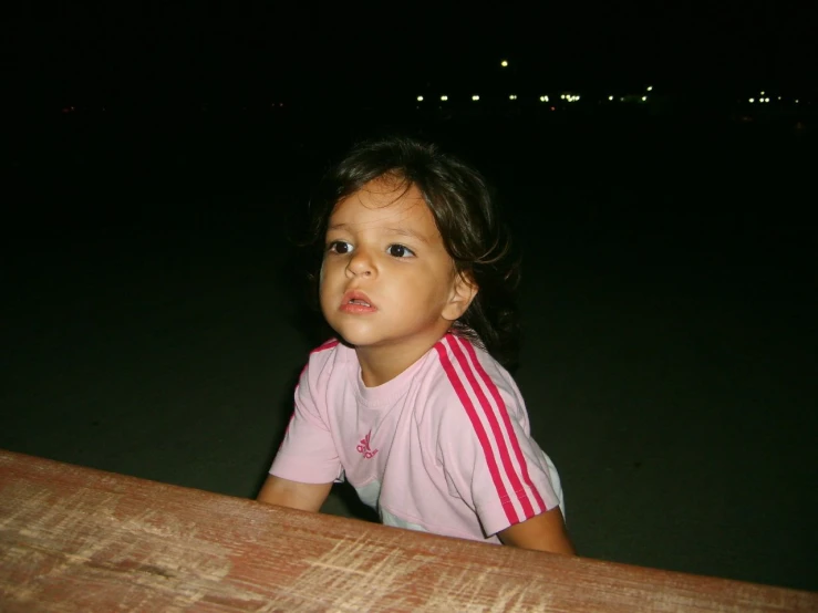 a little girl standing in the dark next to the water