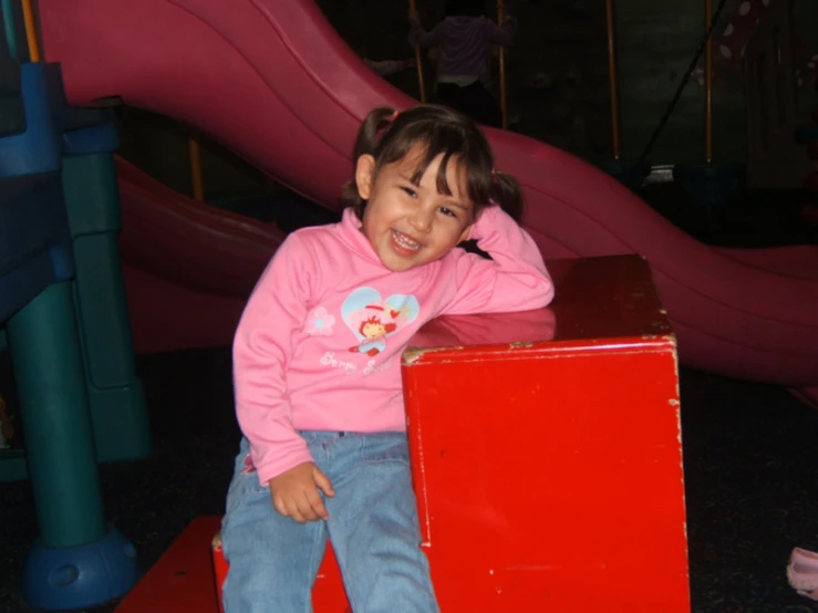 a young child smiles as she sits on top of a red box