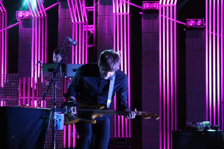 a man playing guitar in front of purple lighting