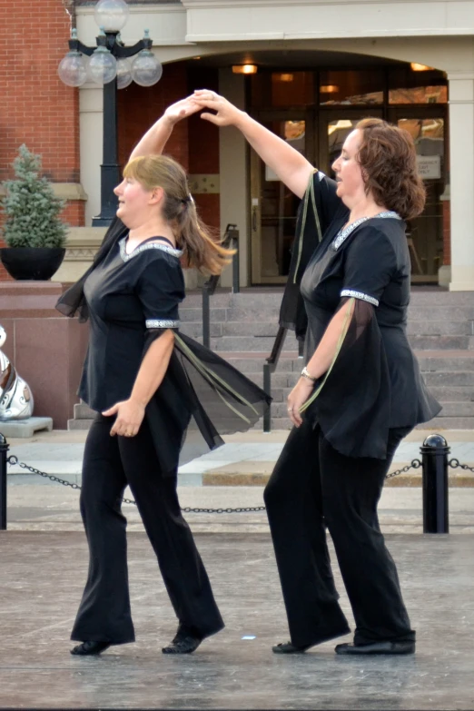 two women dance in the middle of a courtyard in front of a building