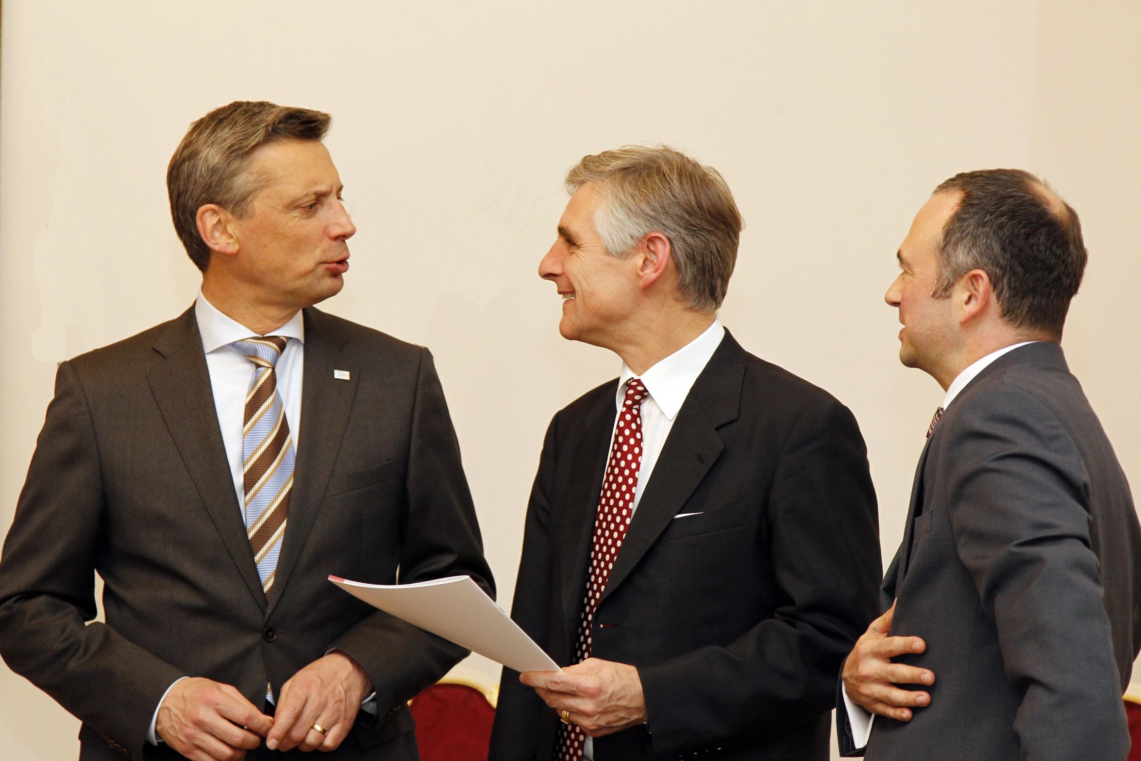 three men dressed in business attire stand in front of a wall