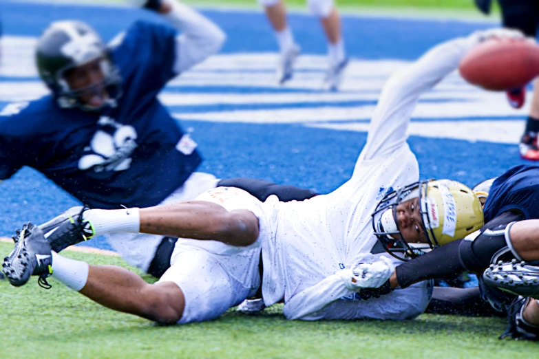 two football players laying on the field with a ball