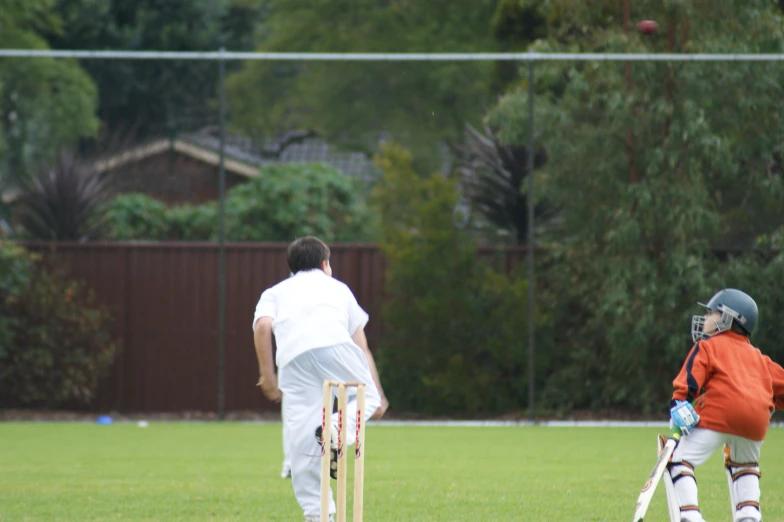 two small children playing with a cricket ball on the field