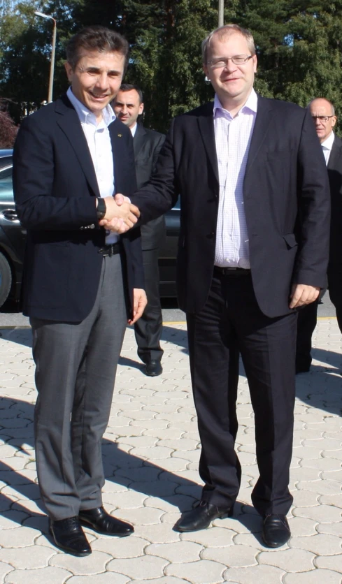 two men shake hands with one another, the other is wearing a suit