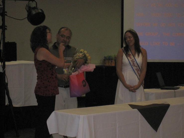 two women stand at the podiums at an event and smile at a man standing behind them