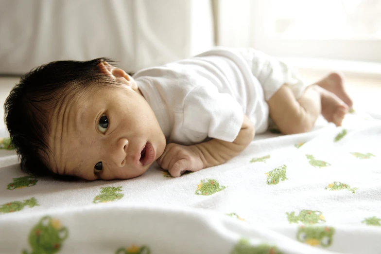 an infant laying on a blanket with a pillow in the background