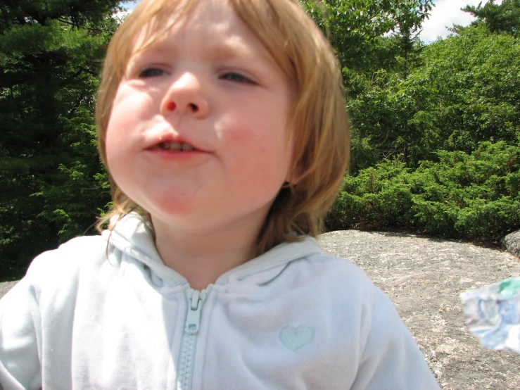 the child is wearing a white robe with trees in the background