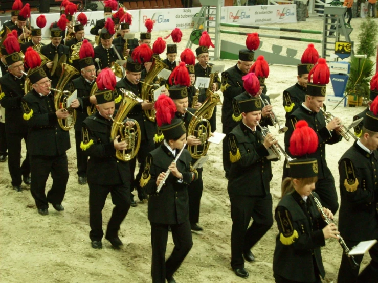 a band with red caps in uniforms marching on the sandy ground