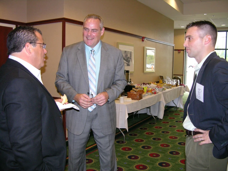 two men in suits talking to another man at a buffet table