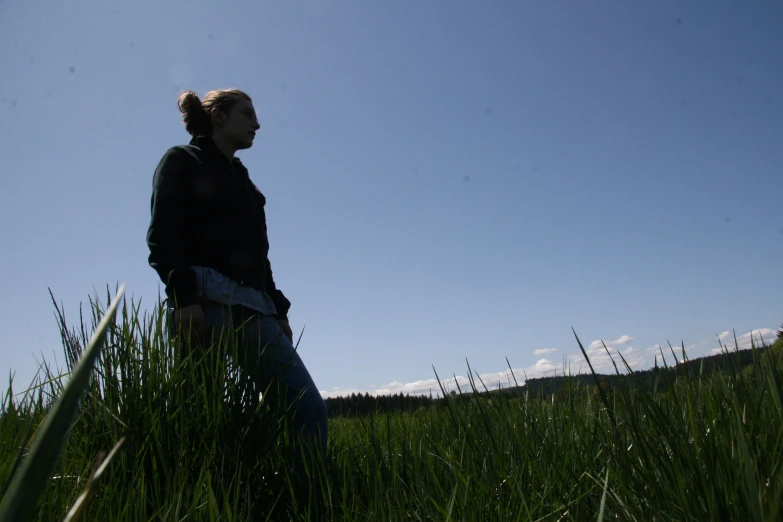 a person standing in tall grass near a hill