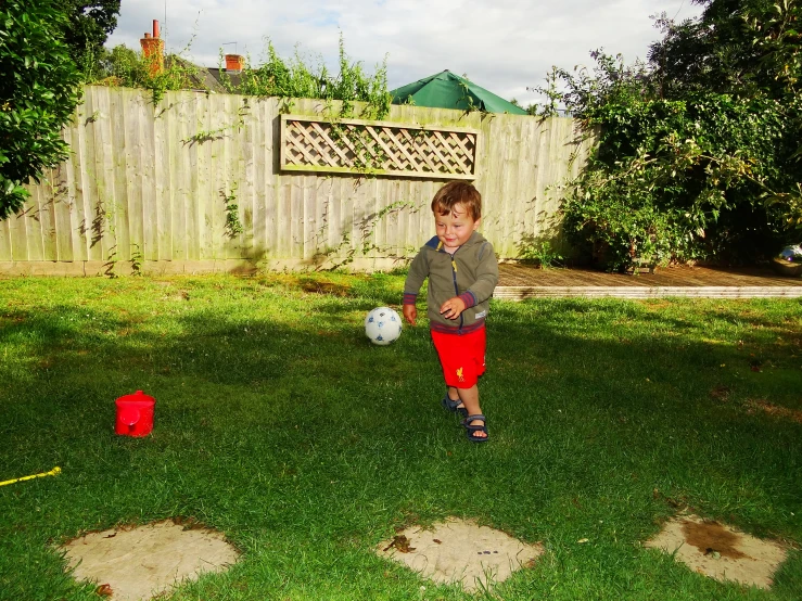 small boy standing on grass in backyard near ball and tee