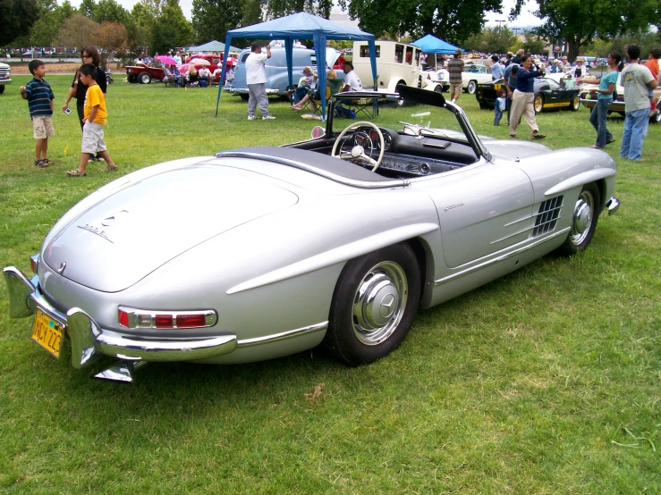 a vintage sports car at an event with some people in the background