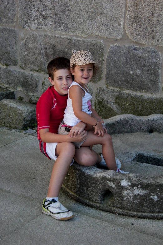 two children sitting on a stone wall