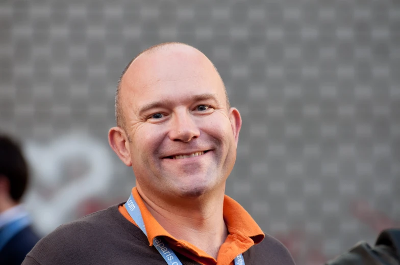 man in an orange shirt with grey collar smiling