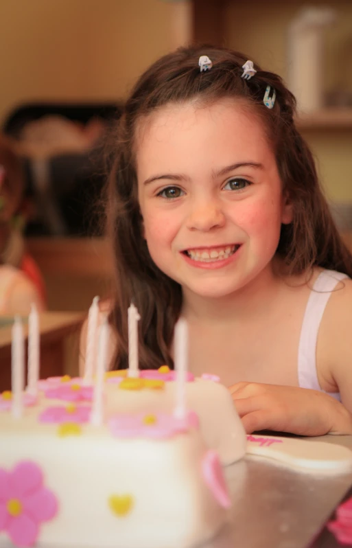 a little girl sitting in front of a birthday cake with pink flowers on it