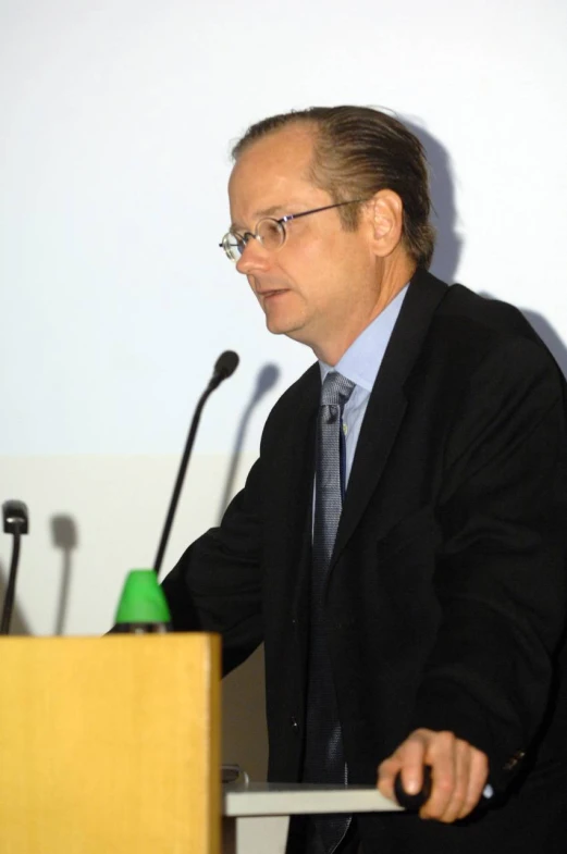 a man sitting at a podium with microphones near him