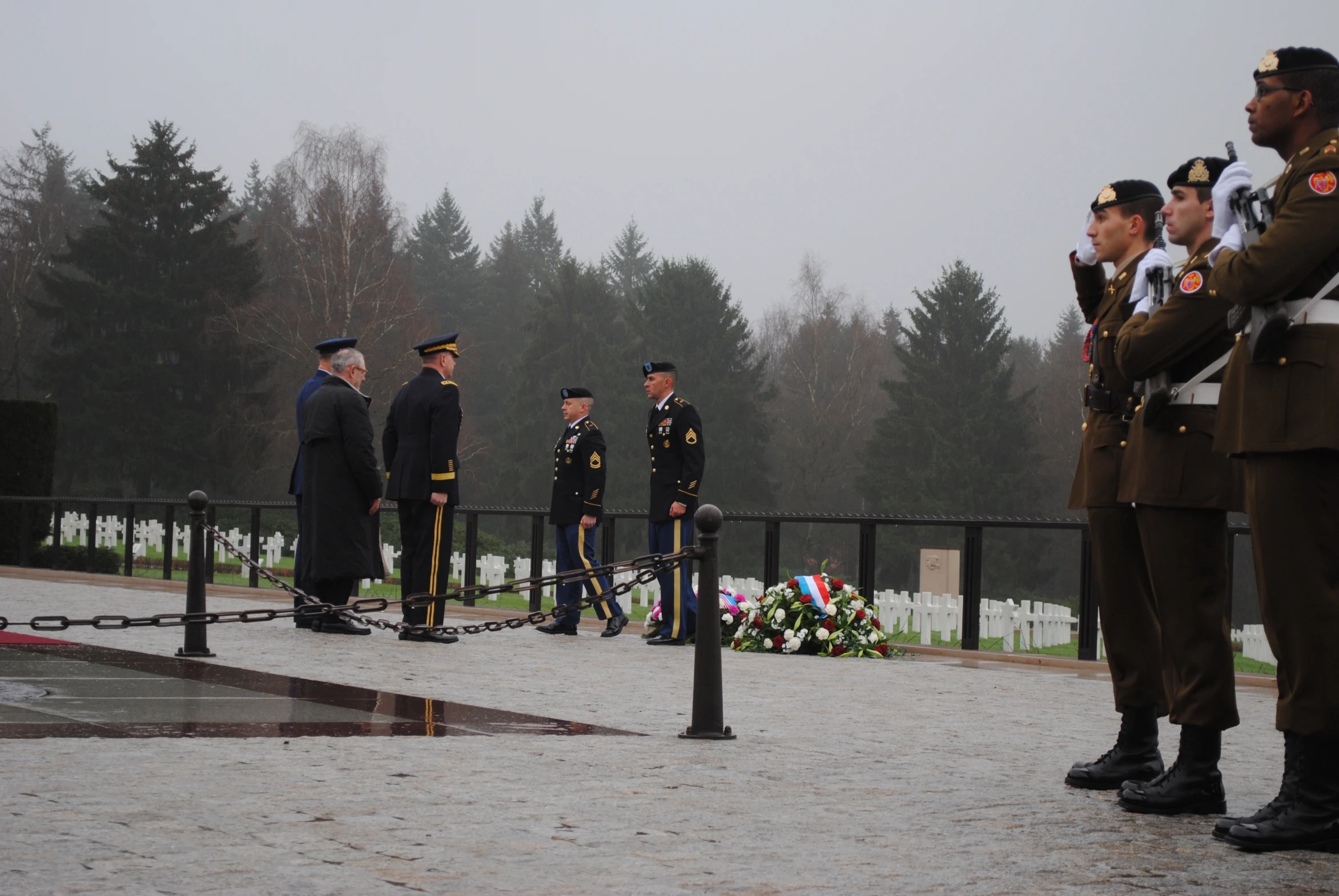 some military men in uniform standing by a flag and wreath