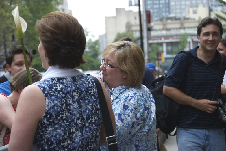 two women stand and talk with others on the sidewalk