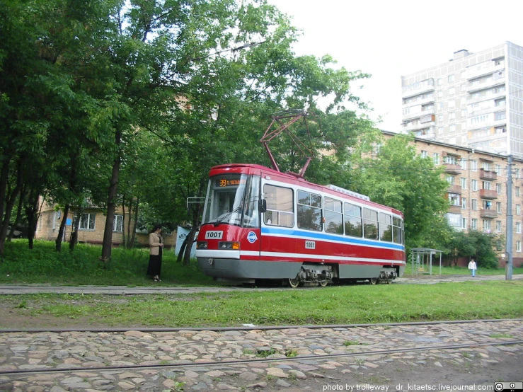 a red, white, and blue trolley car sitting in front of tall buildings