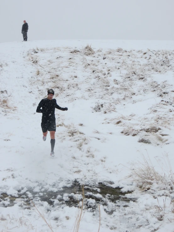 two people walking through snow with a snowy hillside in the background