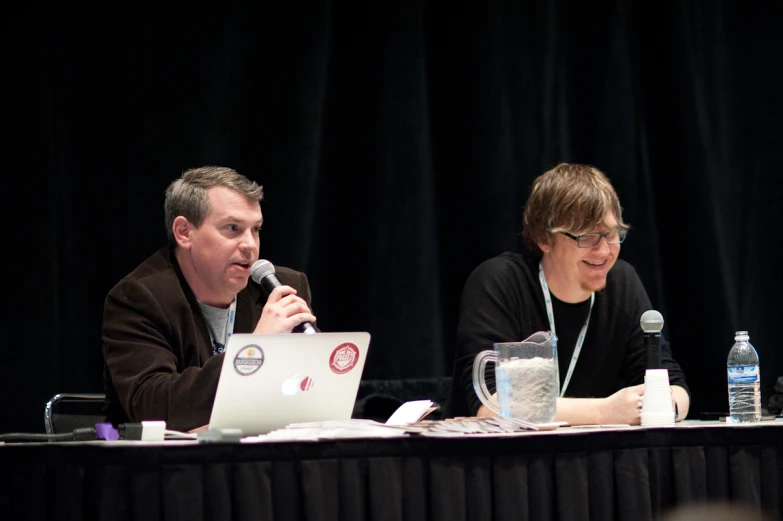 two men are at a meeting with laptops and water bottles