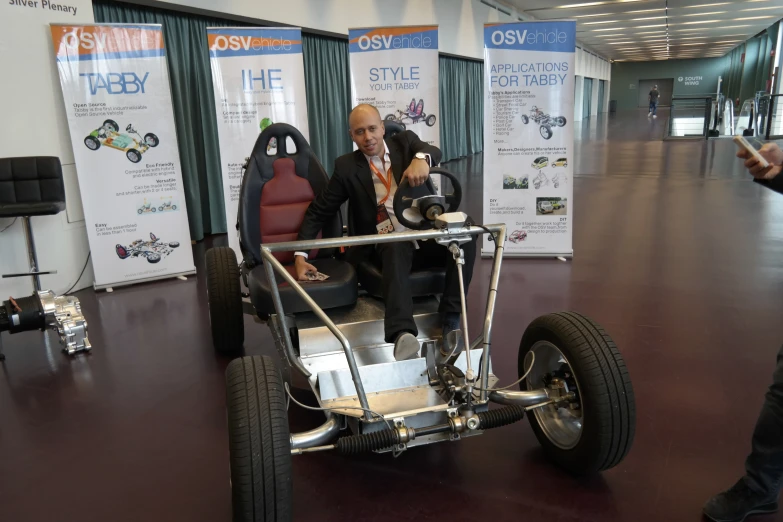 a man sitting in an aluminum race car in a large room