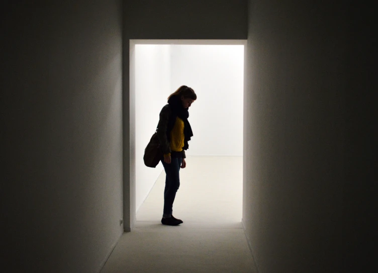 a woman standing in a white room looking into a doorway