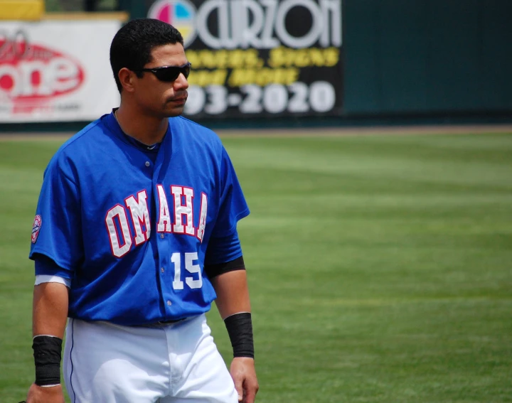 baseball player wearing blue jersey standing on field in front of wall