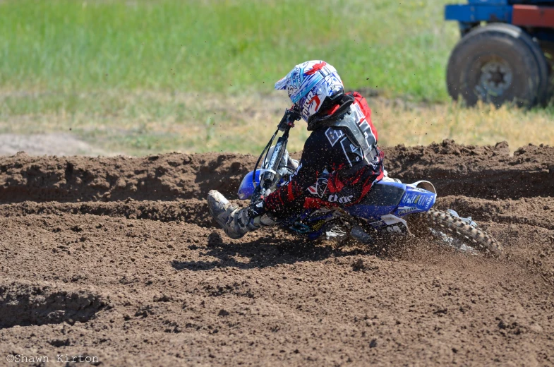 a motorcyclist in a helmet and white and blue jacket, rides over dirt and rocks