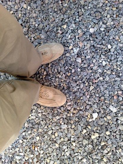 a person in brown shoes standing on a gravel ground