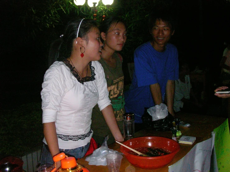 a group of people stand at a table, near a bowl of food