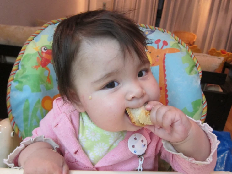 a baby girl is eating food in a high chair