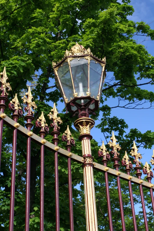 a light on top of an iron fence in front of green trees