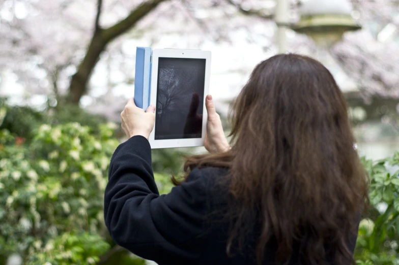 a woman in a dark jacket holds up an electronic device