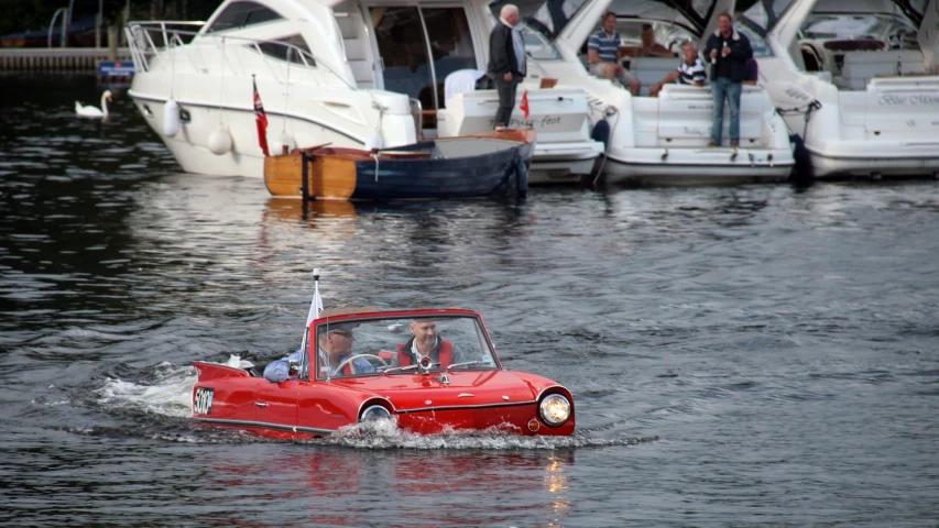 a man driving a small red car across water